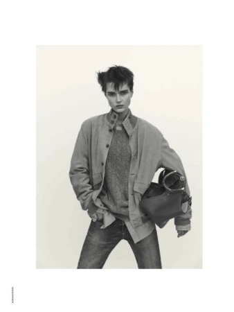 Model wearing a button-down jacket and jeans holding a handbag against a plain background