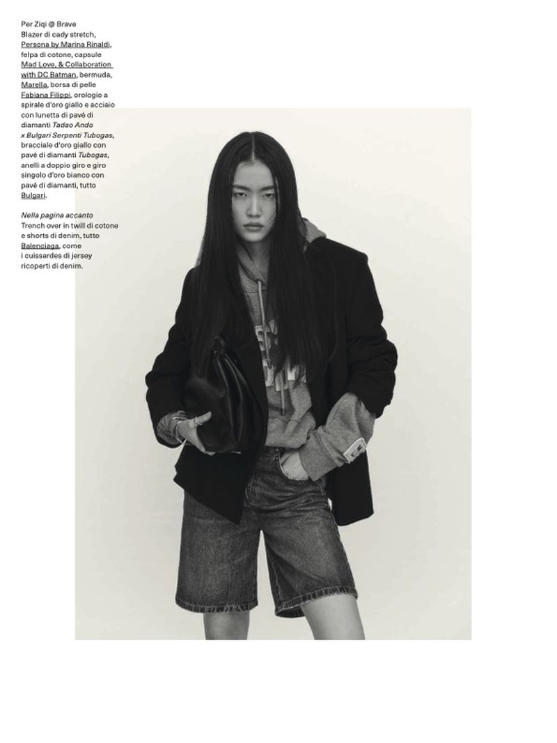 A young Asian woman poses in a fashion editorial shot, wearing a blazer, hoodie, and jean shorts, holding a black purse indoors.