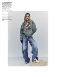 Model standing on a wooden box wearing an oversized green hoodie and wide-leg denim jeans against a plain light background