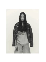 Model wearing a denim jacket and college t-shirt against a plain white studio background for Elle Italia.