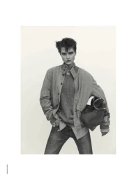 Model wearing a button-down jacket and jeans holding a handbag against a plain background
