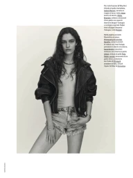Model with long dark wavy hair wearing a black leather jacket and denim shorts against a plain background.
