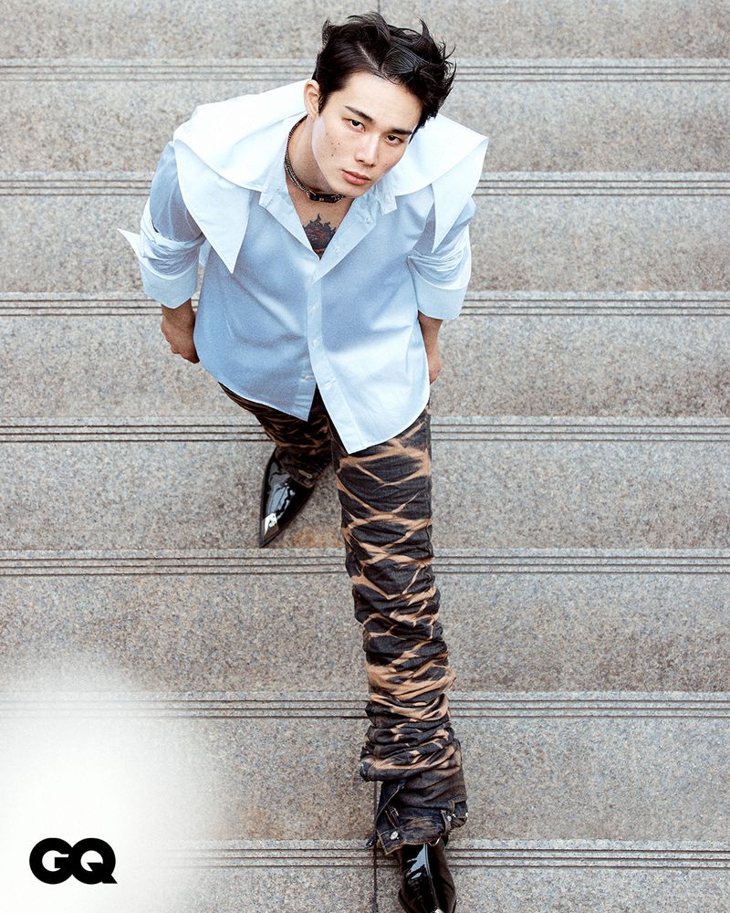 Man on stairs wears a white shirt and unique pants. He is seen from an overhead angle with the GQ logo in the corner.
