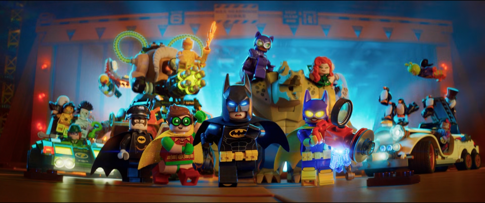 LEGO figures of Batman, Robin, and Batgirl, along with other LEGO characters on a set of LEGO vehicles, under blue lighting.