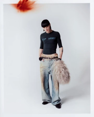 A person in a black long-sleeved shirt with the words 'POP ARMY' and wide-legged jeans is posing in a full shot against a white backdrop.
