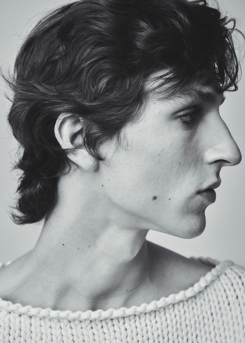 Close-up profile portrait of a male model wearing a textured knit sweater against a plain background