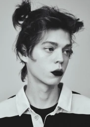 Close-up portrait of a male model with dark lipstick and hair in a top knot wearing a striped collared shirt against a white backdrop.