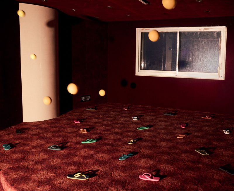 Abstract surreal indoor scene with floating yellow spheres and numerous colorful flip-flops scattered across a red patterned carpet.