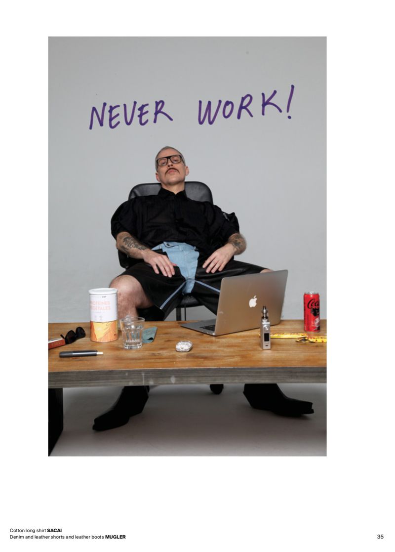 Adult male sits in an office chair at a desk in front of a light gray wall with the words 'Never Work!' written in purple marker.