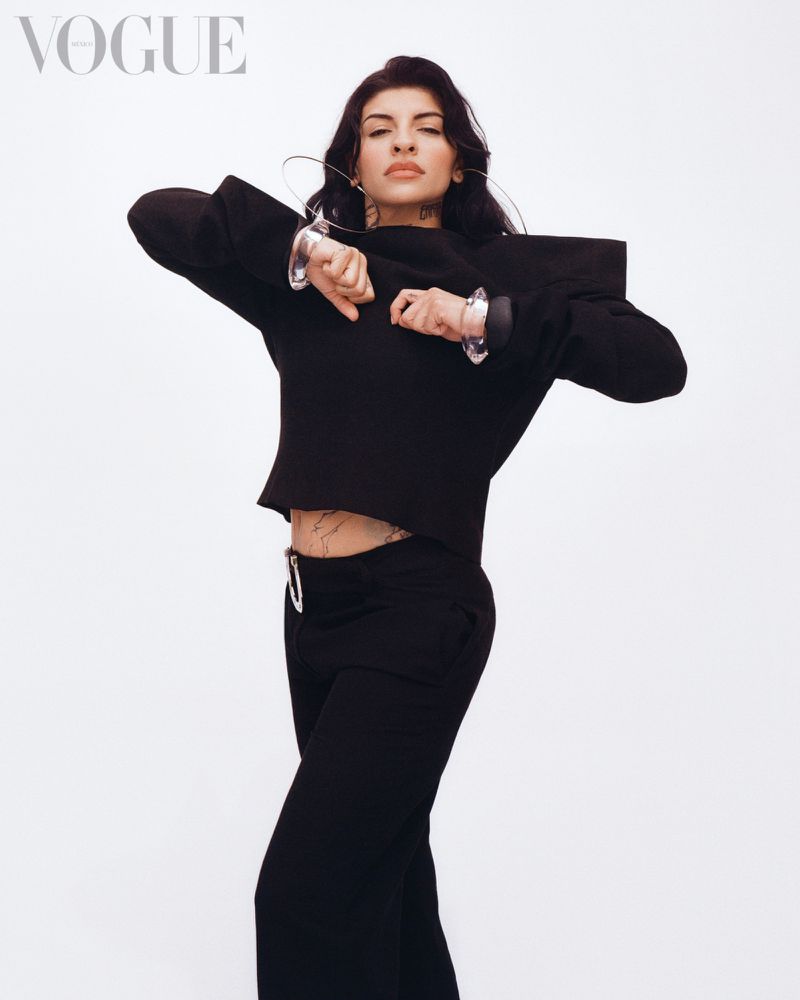 Cazzu wearing a black structured top and pants against a white background for Vogue Mexico