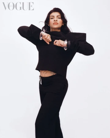 Cazzu wearing a black structured top and pants against a white background for Vogue Mexico