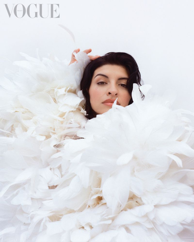 Brunette woman poses in a close-up shot wearing a white feathered dress, set against a bright white background for a Vogue fashion editorial.