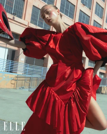 Model wearing a vibrant red dress with voluminous puff sleeves outdoors against a brick building exterior.