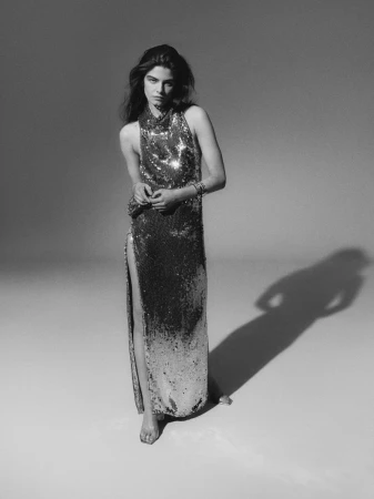 Model Merlijne Schorren wearing a sequined slip dress standing against a grey studio seamless background.