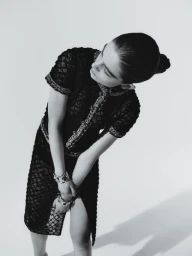 Model Merlijne Schorren wearing a black lace dress with metallic bracelets against a white seamless background