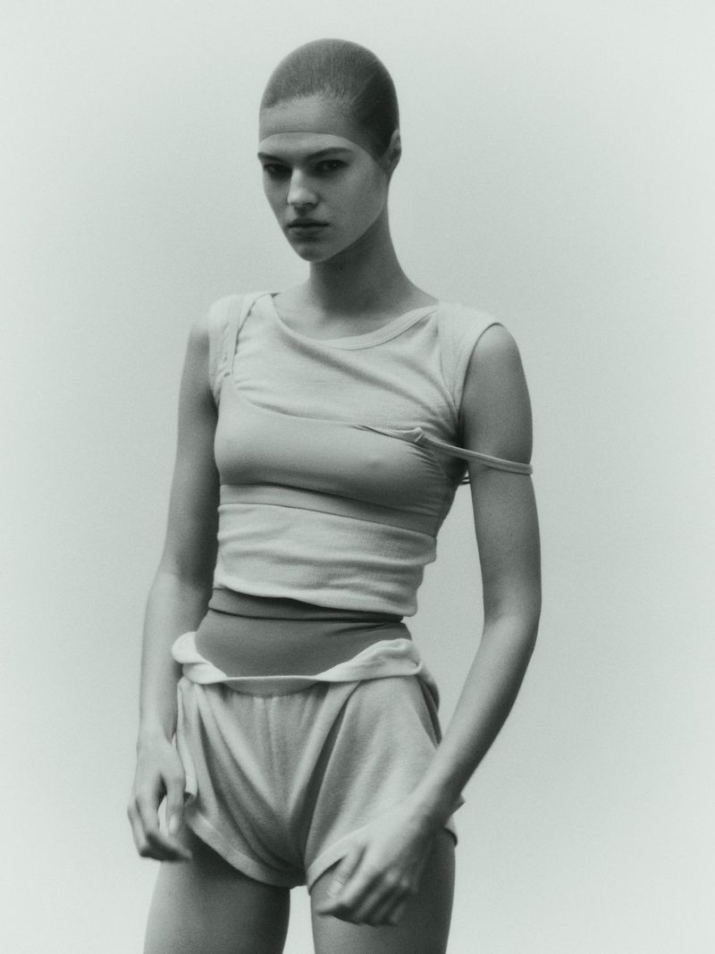 Model with short hair wearing a light-colored sleeveless top and shorts against a neutral studio background