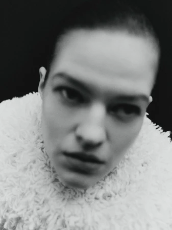 Monochrome portrait of a woman with short hair wearing a textured white coat, set against a stark black background.