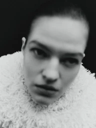 Close-up portrait of a model wearing a textured white garment against a dark background.