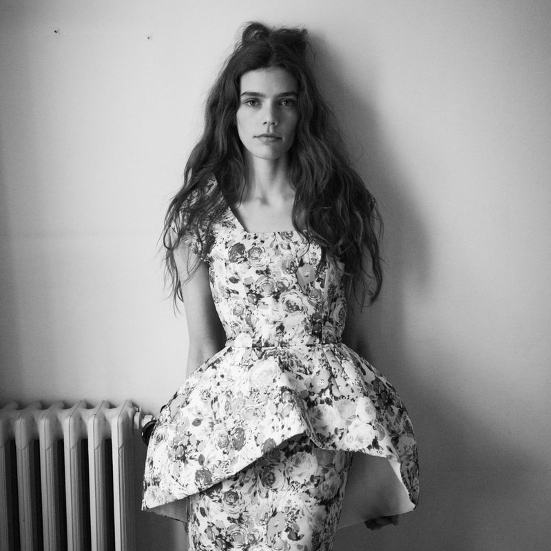 Model in a floral print peplum dress posing against a plain wall next to a radiator.