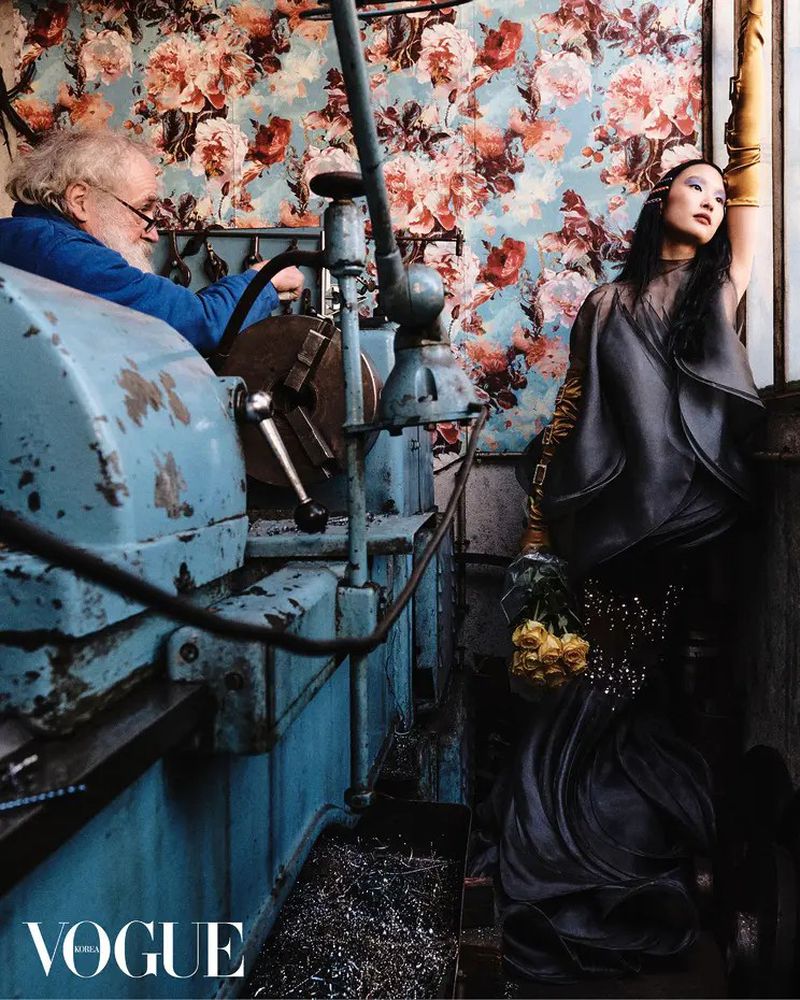 Editorial shot: An older man operates machinery in front of a floral wall, juxtaposed with a stylish woman in a dark dress and yellow roses.