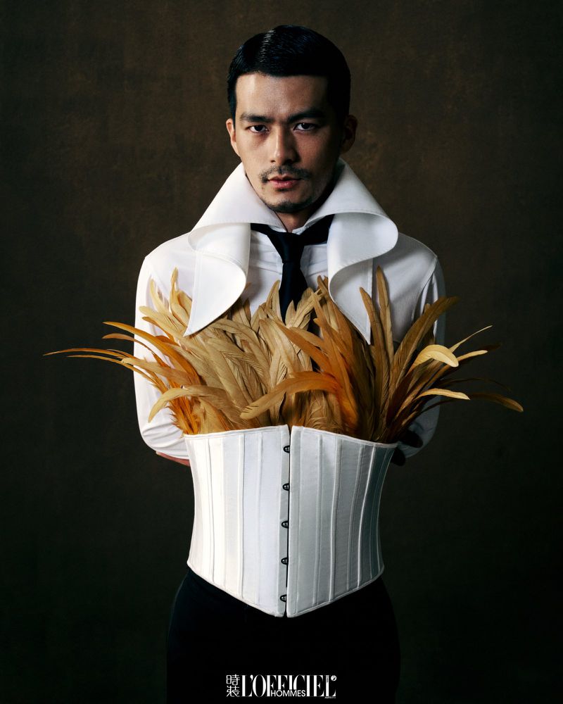 Man wearing a white shirt with a high collar, corset, and protruding golden feathers for L'Officiel Hommes China project