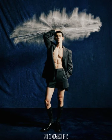 Model standing against textured dark blue background holding a fan shaped burst of white particles overhead.