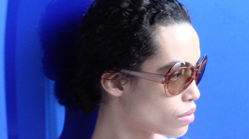 Model Lara Menezes wearing tinted sunglasses against a vibrant blue studio background for POP Magazine