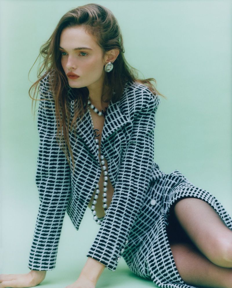 Model Lulu Tenney in a black and white patterned jacket and skirt with a long pearl necklace against a pale green backdrop.