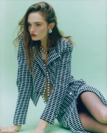 Model Lulu Tenney in a black and white patterned jacket and skirt with a long pearl necklace against a pale green backdrop.