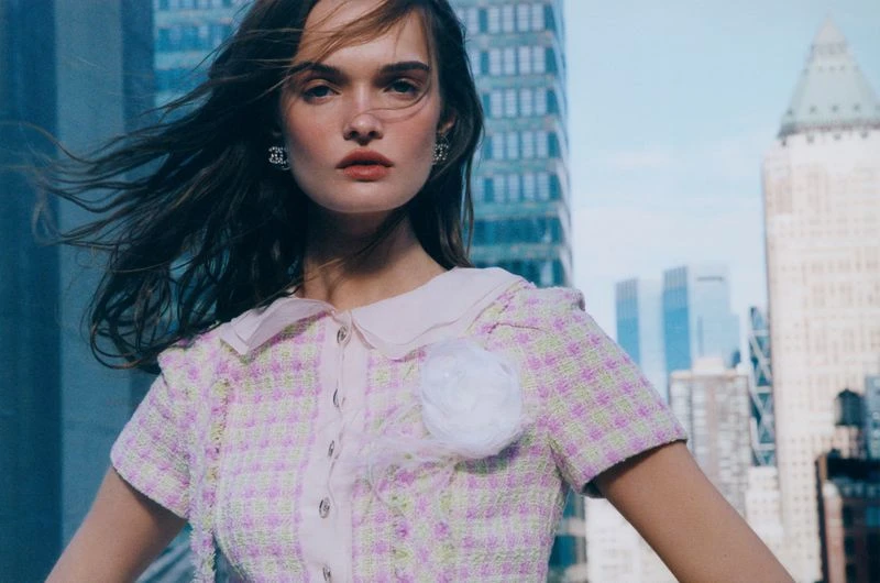 Fashion portrait of a woman in a pink tweed jacket with windblown hair and city buildings in the background, fashion and beauty.