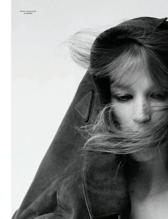 Close-up monochrome portrait of model Jacqui Hooper with hair blowing across her face wearing a brown jacket against a white background