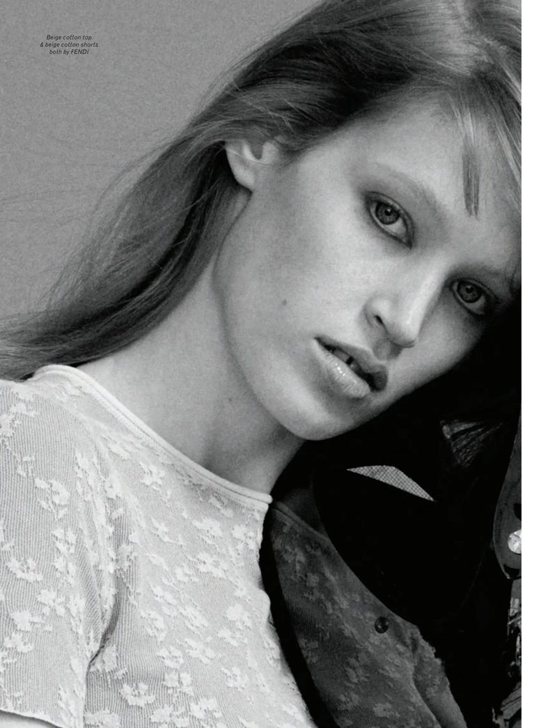 Close-up portrait of model Jacqui Hooper wearing a white patterned top against a plain textured grey background.