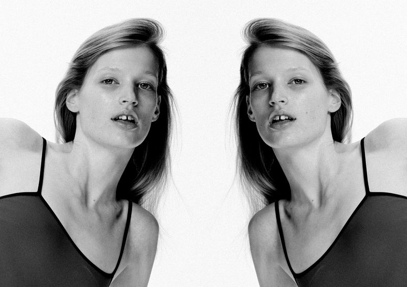 Monochrome portrait of a young fair-skinned woman with straight blonde hair, wearing a tank top, duplicated against a bright white backdrop.