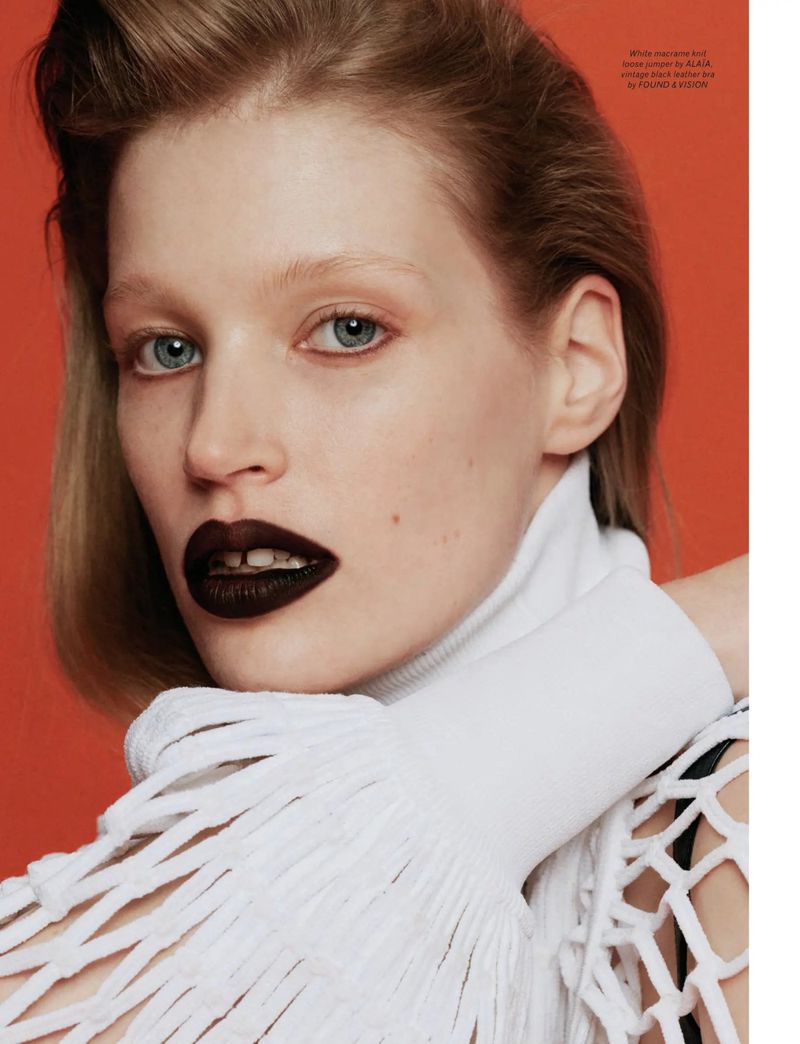 A close-up of a blonde female fashion model with a white, textured top, set against an orange background. Bold, dark lipstick.