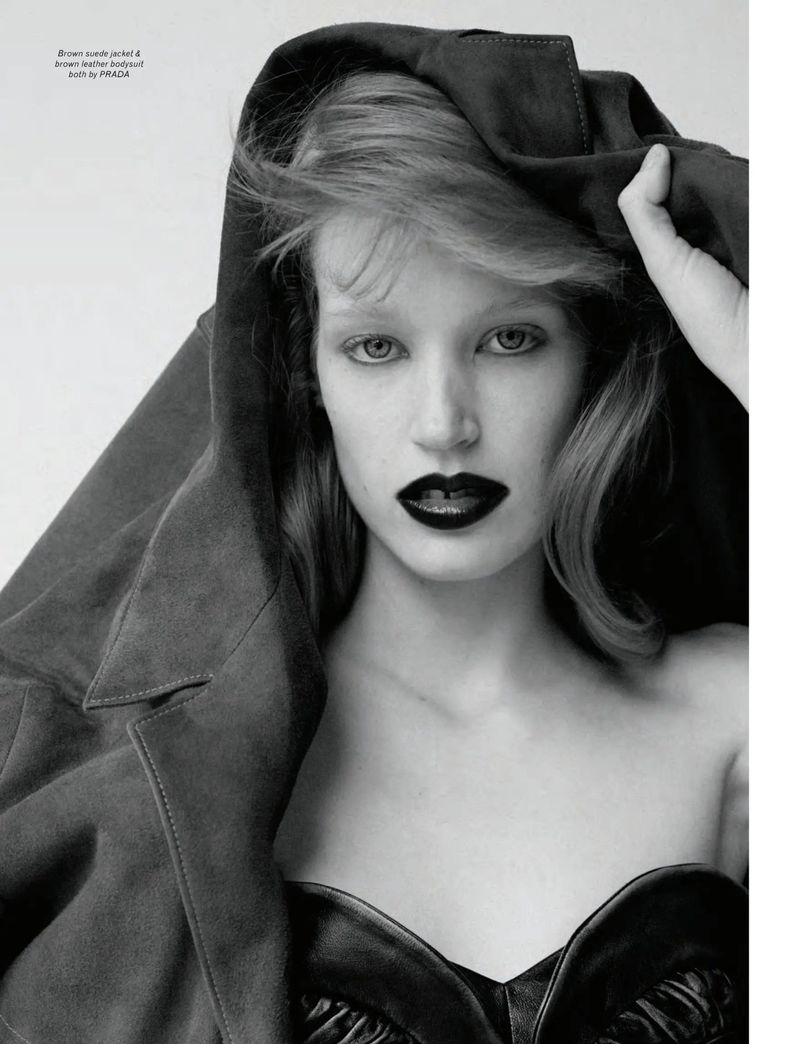 Monochrome portrait of model Jacqui Hooper in dark lipstick pulling a heavy suede jacket over her head against a plain white studio backdrop.