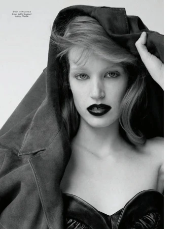 Monochrome portrait of model Jacqui Hooper in dark lipstick pulling a heavy suede jacket over her head against a plain white studio backdrop.