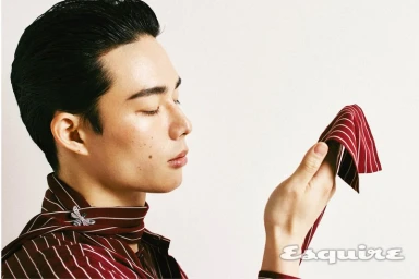 Model Joji Iwase wearing a burgundy striped shirt and jewelled brooch, holding a red striped fabric for Esquire Korea.