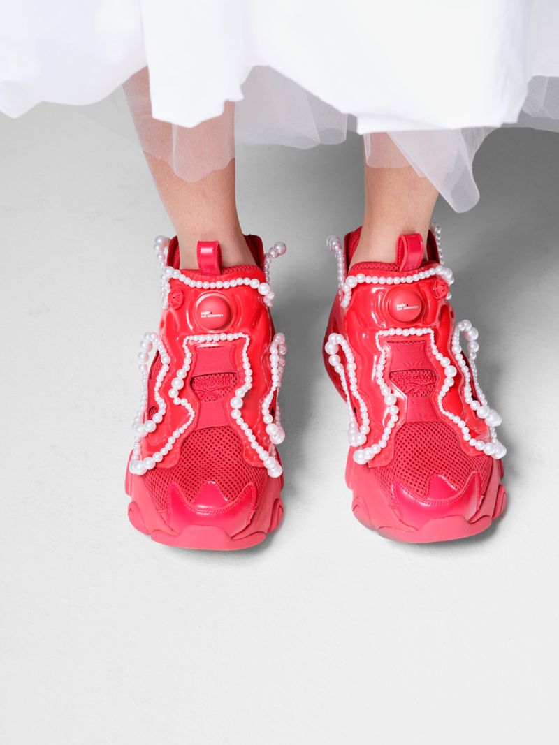 Child's feet in red sneakers with pearl embellishments, set against a plain white backdrop, showcasing a blend of style and detail.