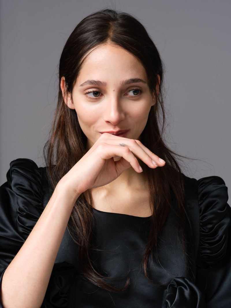 Close-up portrait of model Yasmin Wijnaldum wearing a black satin top against a solid grey background for At Large Magazine.