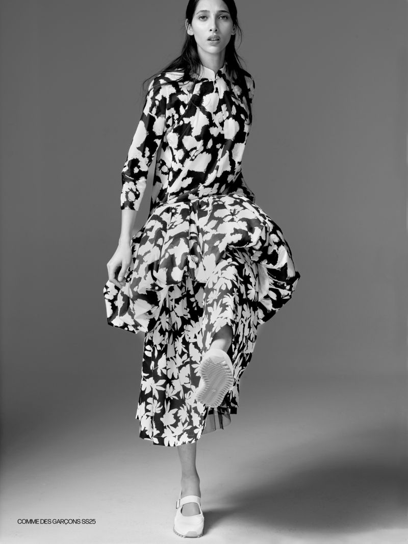 Monochrome fashion shot of a woman in a patterned midi dress and white mary jane shoes, striking a pose in a photo studio setting.