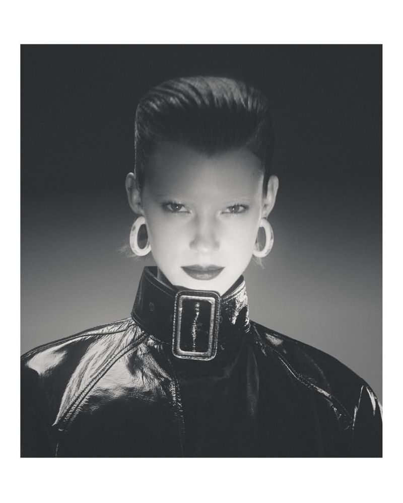 Glamour headshot of a stylish woman in a high-fashion black patent-leather jacket with oversized earrings, set against a diffused background.