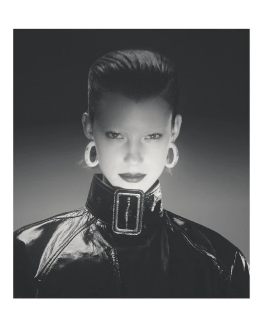 Glamour headshot of a stylish woman in a high-fashion black patent-leather jacket with oversized earrings, set against a diffused background.
