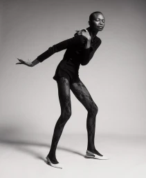 Black model Debra Shaw posing in dark attire and patterned tights against a gradient grey studio backdrop for 212 Magazine cover story