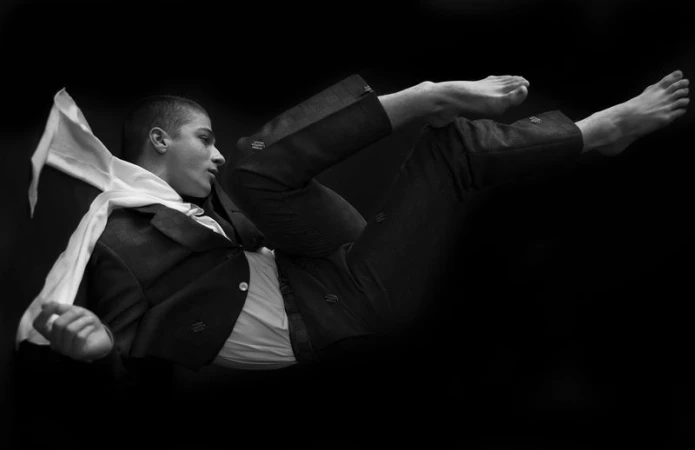 Black and white portrait of a young man wearing a dark jacket and trousers floating against a dark background.