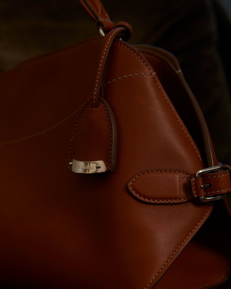Close-up studio shot of a brown leather handbag with silver hardware details, showcasing fashion accessory with soft, diffused lighting.