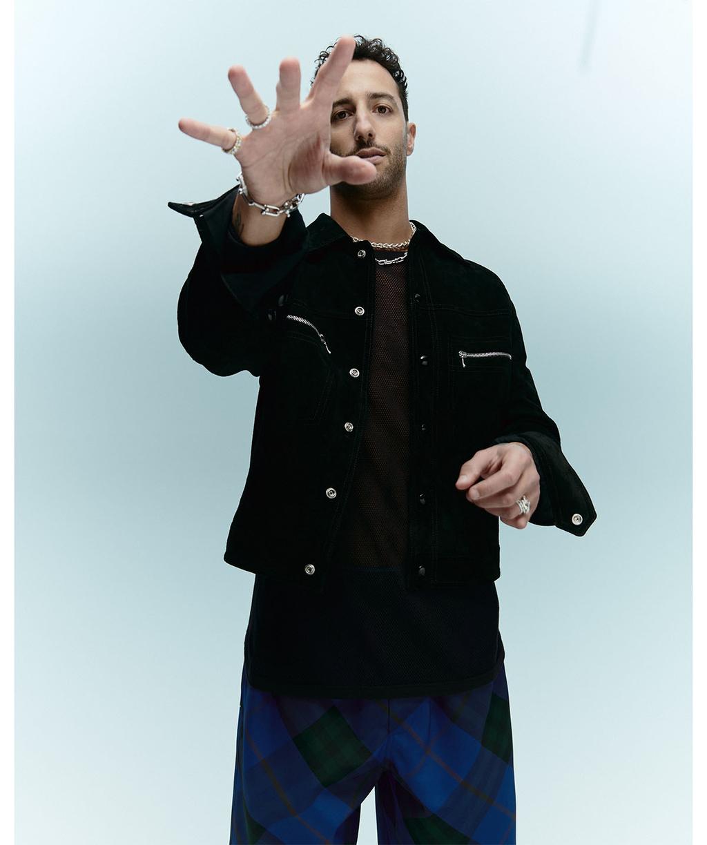 Daniel Ricciardo in a black jacket reaching toward the camera against a light grey studio background for GQ Australia.