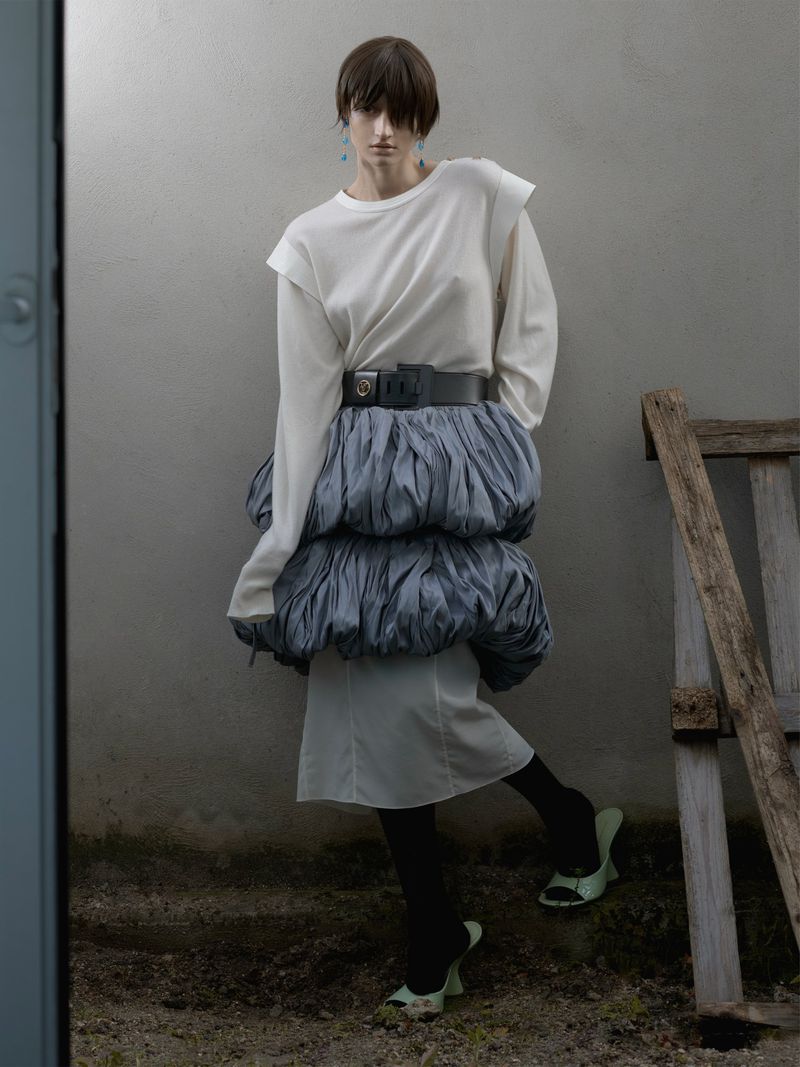 Fashion model in a white long-sleeve top and a tiered blue ruffle skirt with black tights and mint heels poses outdoors.