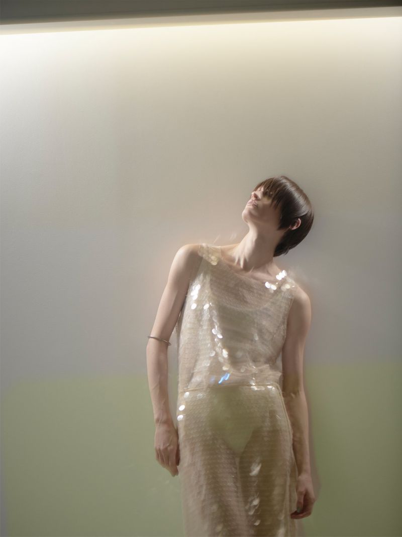 Adult woman in a sequin dress looking up toward a light with soft focus and color grading in an indoor environment, in a fashion style.
