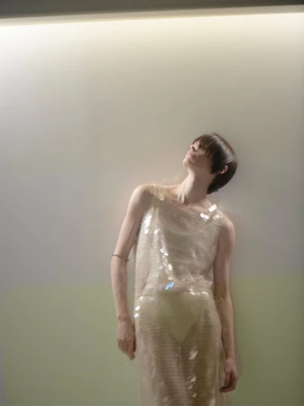Adult woman in a sequin dress looking up toward a light with soft focus and color grading in an indoor environment, in a fashion style.