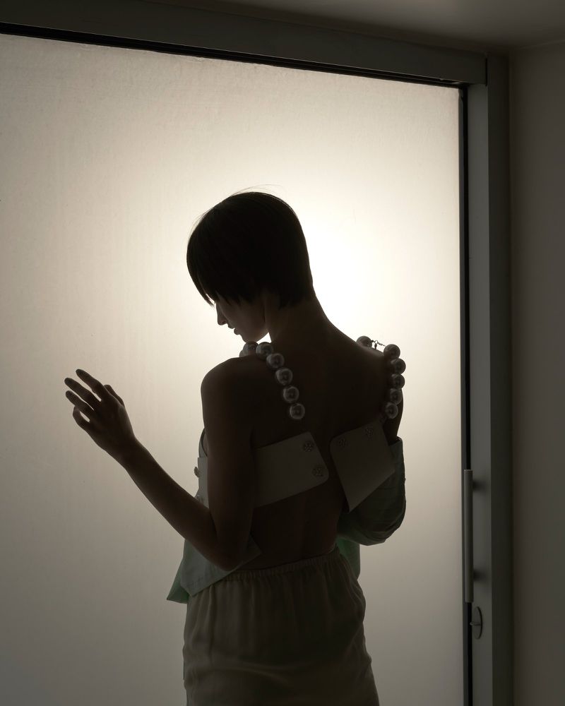 Back view of a slender adult woman with bobbed hair wearing a pearl strap top and loose-fitting pants in a studio environment.
